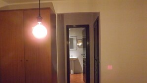 Un couloir étroit, avec une porte en bois sur la gauche et une salle de bain visible à travers une porte ouverte.