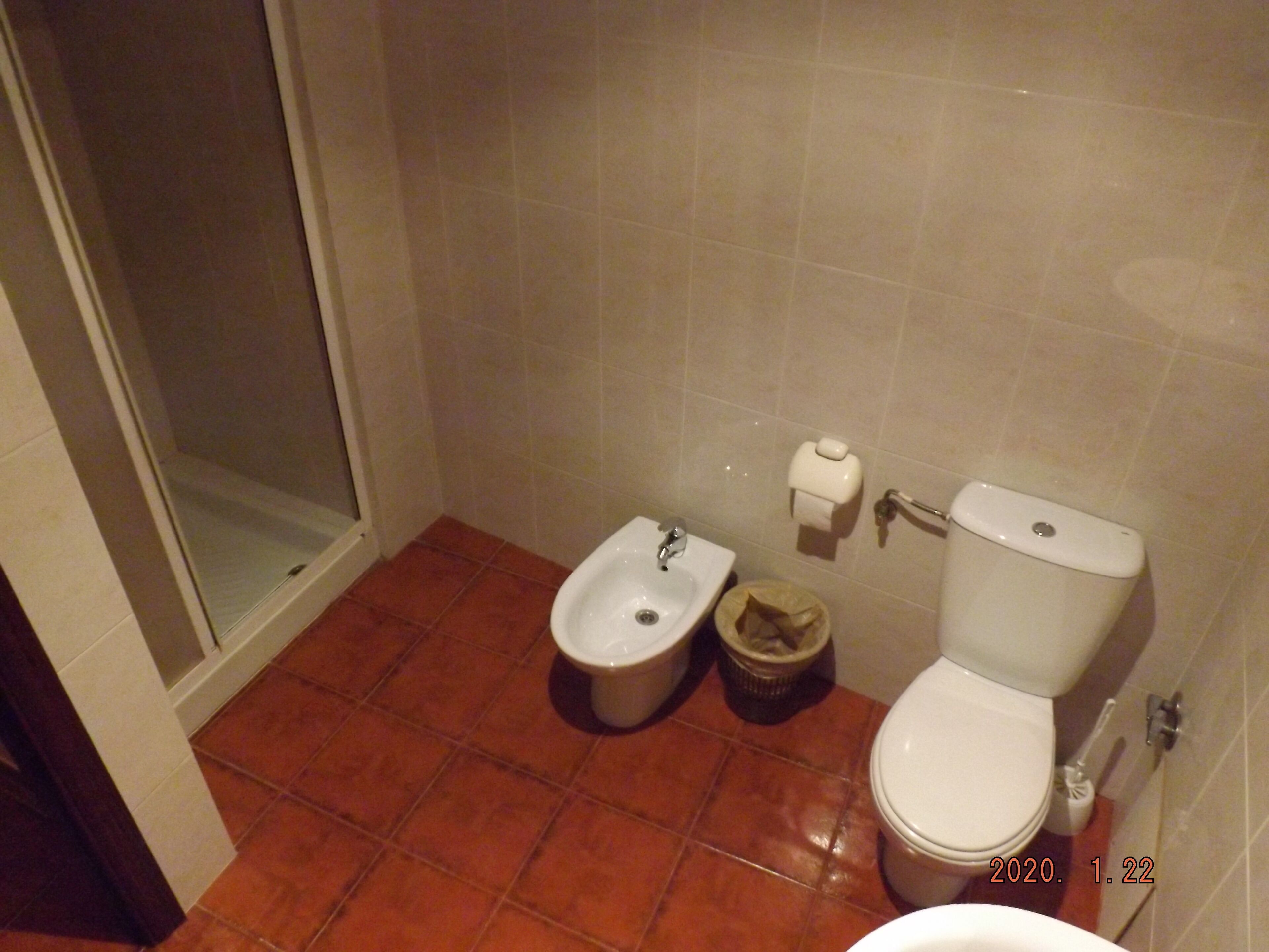 A bathroom with a shower, a bidet, a toilet, and a trash bin.