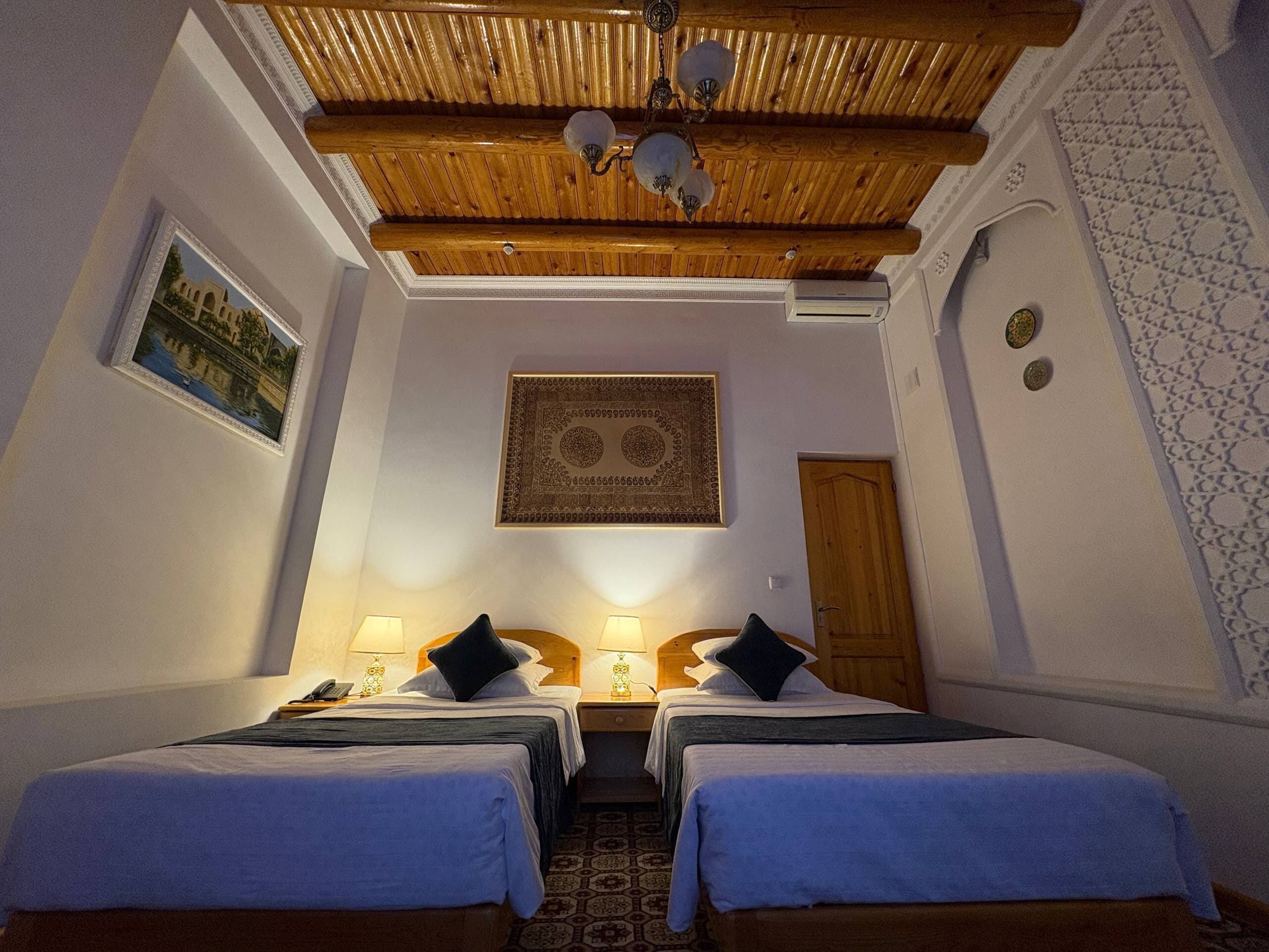 A hotel room with two beds, a wooden ceiling, a patterned wall, and a door.