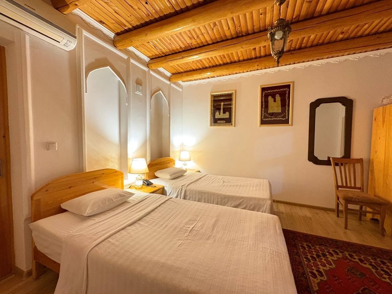 Une chambre avec deux lits, des têtes de lit en bois, un plafond en bois, un miroir et une chaise.