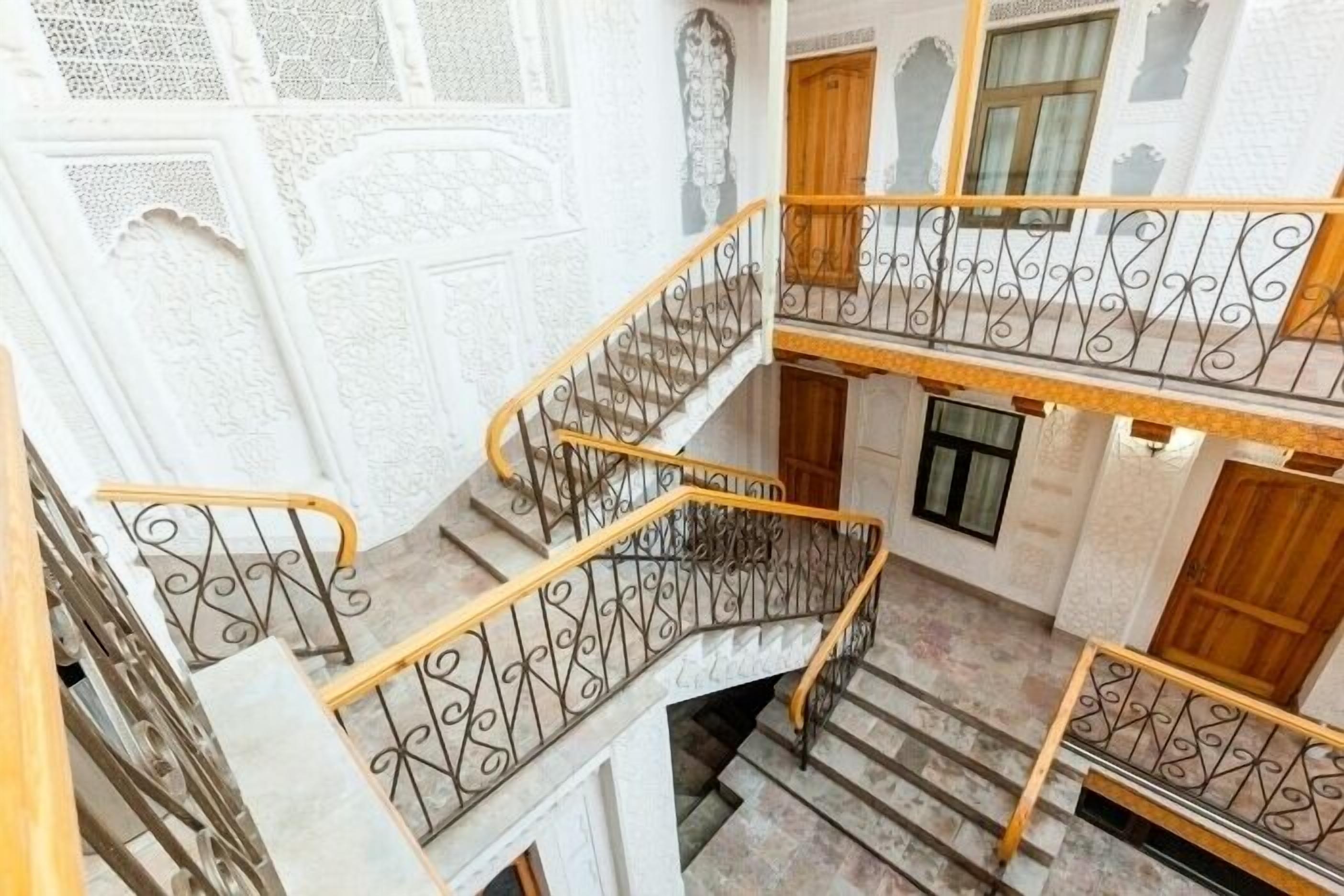 A multi-level interior with ornate white walls, a central staircase with wrought iron railings, and a wooden door at the top.