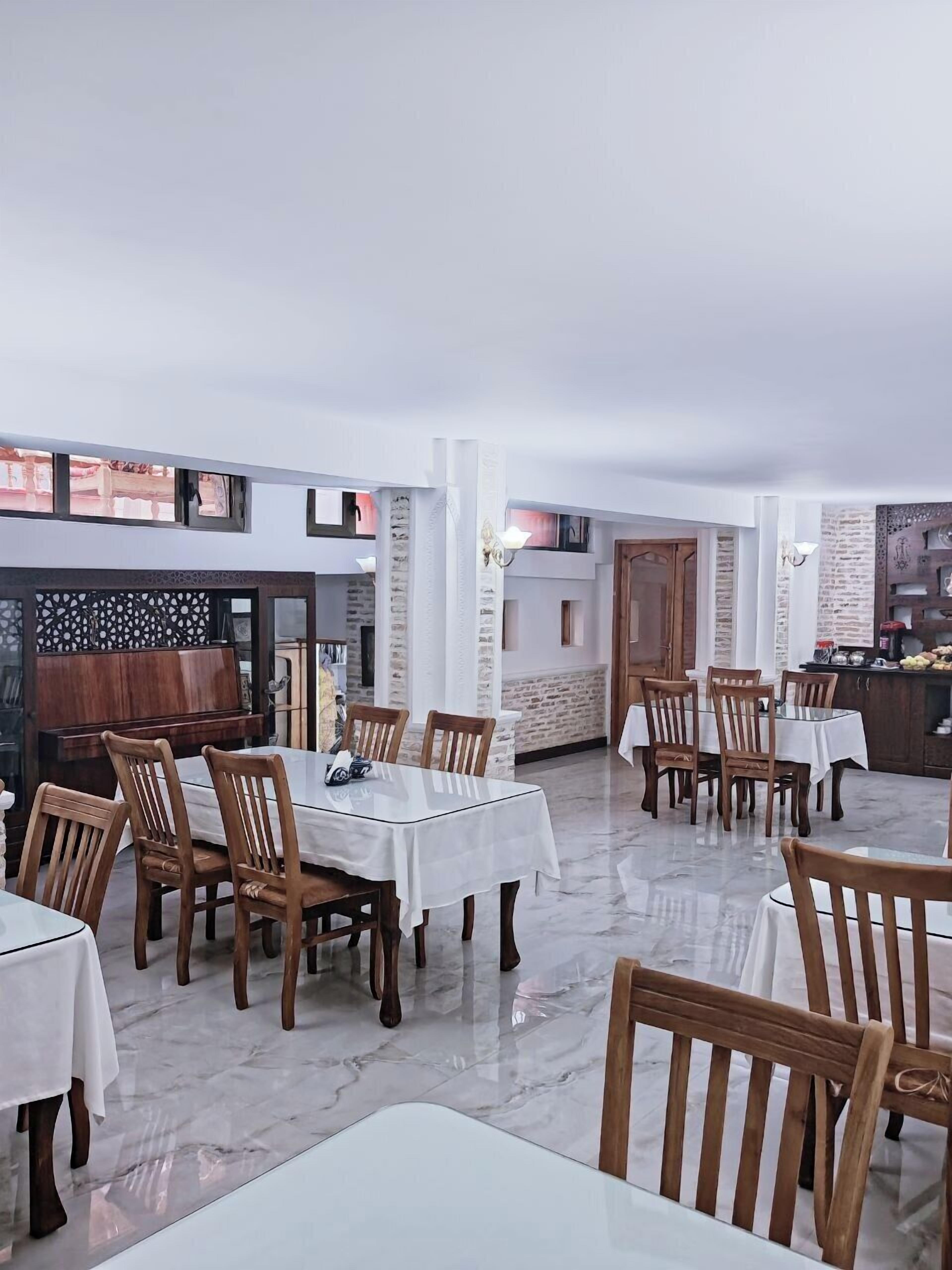 A dining area with marble flooring, wooden chairs, and tables covered with white tablecloths.