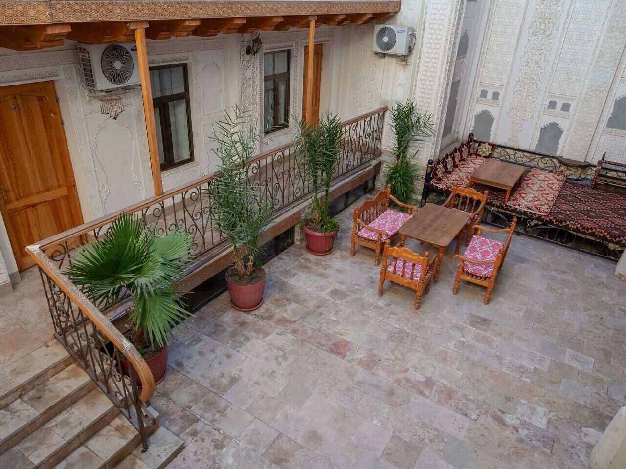 Een binnentuin met een houten trap, plantenpotten en een terras met een tafelkleed met dessin.