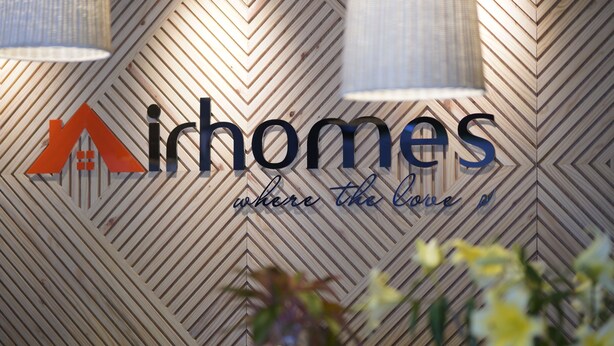 Ein Schild mit dem Text „Airhomes“ und einem Logo vor einer Holzwand mit Zickzackmuster.