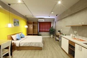 A compact hotel room with a bed, bedside table, and a small desk. There is a kitchenette with a sink and a potted plant. - Hotel Airhomes (Ho Chi Minh City)