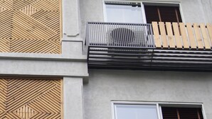 Ein mehrstöckiges Gebäude mit einer geometrischen Holzfassade, Balkonen mit Metallgeländern und einer Betonaußenwand.