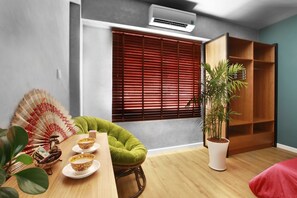 A room with a wooden dining table, a green chair, a fan, a potted plant, and a window with blinds. - Hotel Airhomes (Ho Chi Minh City)
