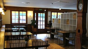 A restaurant with wooden tables and chairs, a clock, and a view through the windows. - Hôtel des Haudères (Evolène)