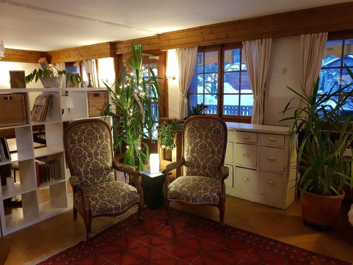 A cozy room with two patterned armchairs, a bookshelf, a potted plant, and a window with curtains.