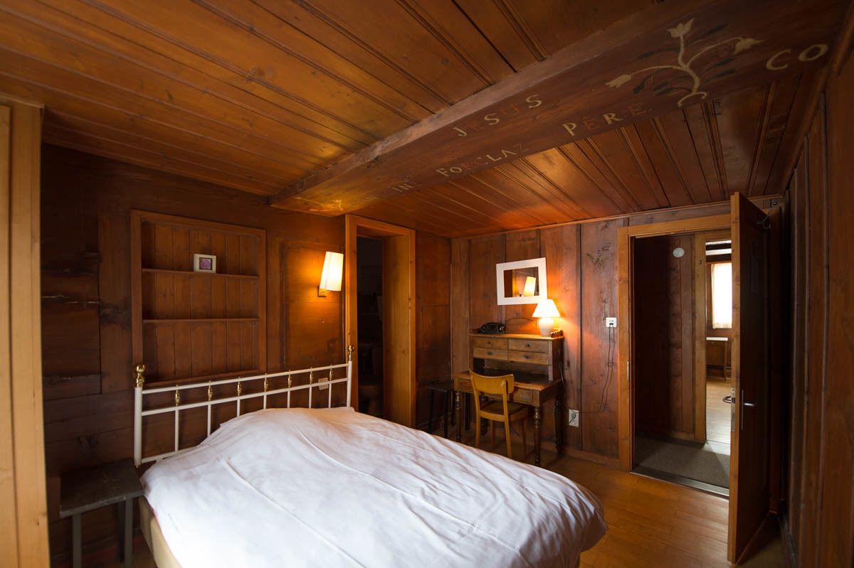 A wooden cabin room with a bed, a desk, and a chair.