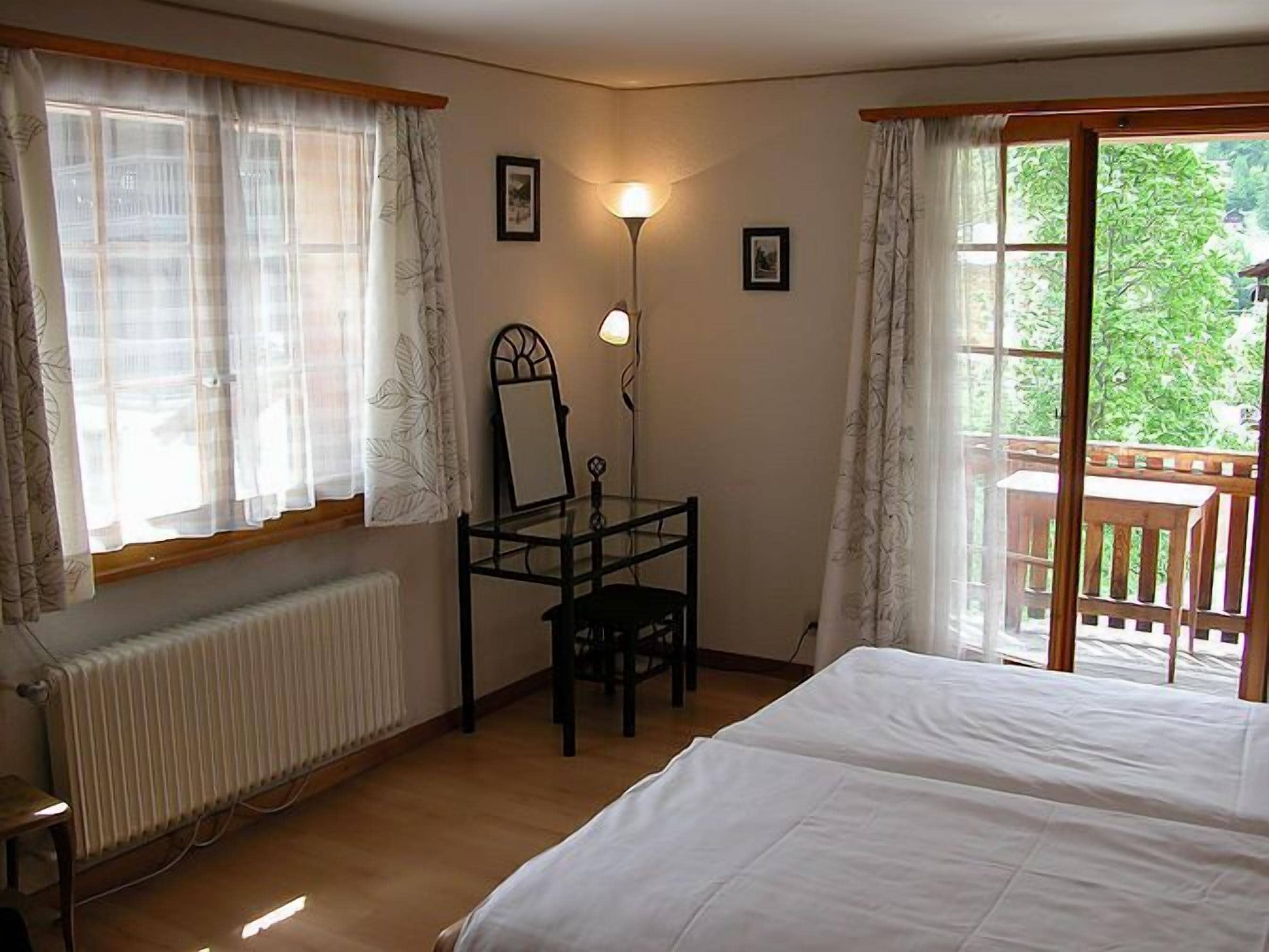 Ein Schlafzimmer mit Bett, Schreibtisch mit Stuhl, Heizkörper und Fenster mit Vorhängen.