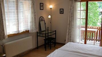 Ein Schlafzimmer mit Bett, Schreibtisch mit Stuhl, Heizkörper und Fenster mit Vorhängen.