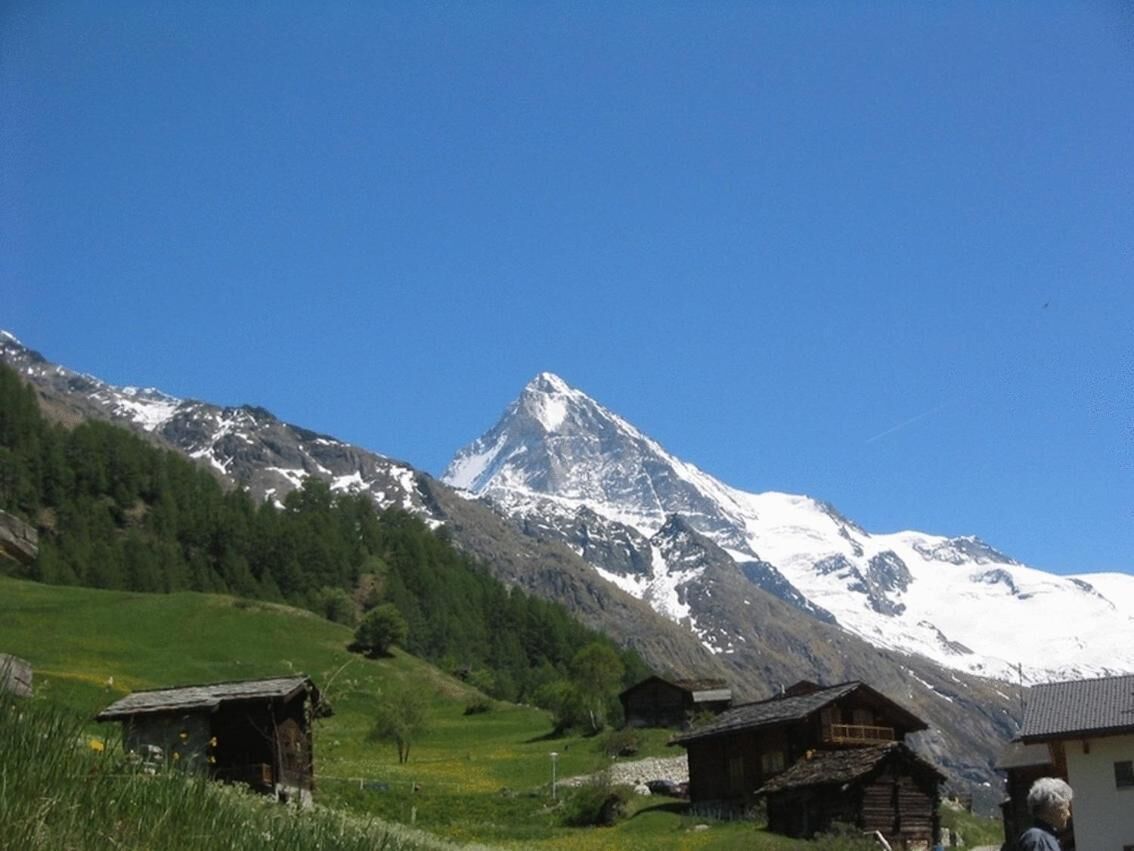 Eine Berglandschaft mit einem markanten Gipfel, umgeben von grünen Feldern und Holzhäusern.