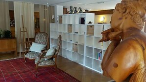 A room with a large wooden statue, a patterned armchair, a white shelving unit, and a red carpet. - Hôtel des Haudères (Evolène)