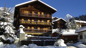 A hotel with a wooden facade and balconies, surrounded by snow-covered trees and mountains. - Hôtel des Haudères (Evolène)