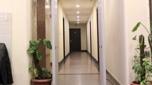 A hallway with a brown mat at the entrance, potted plants on either side, and a vending machine labeled 'VEGA' at the end. - Hotel Marigold (New Delhi)