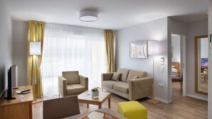 Een moderne hotelkamer met een bank, fauteuil, eettafel en een televisie.