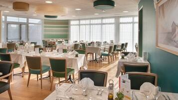 A dining area with multiple tables set for service, chairs, and a large window providing natural light.