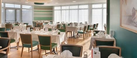 A dining area with multiple tables set for service, chairs, and a large window providing natural light.