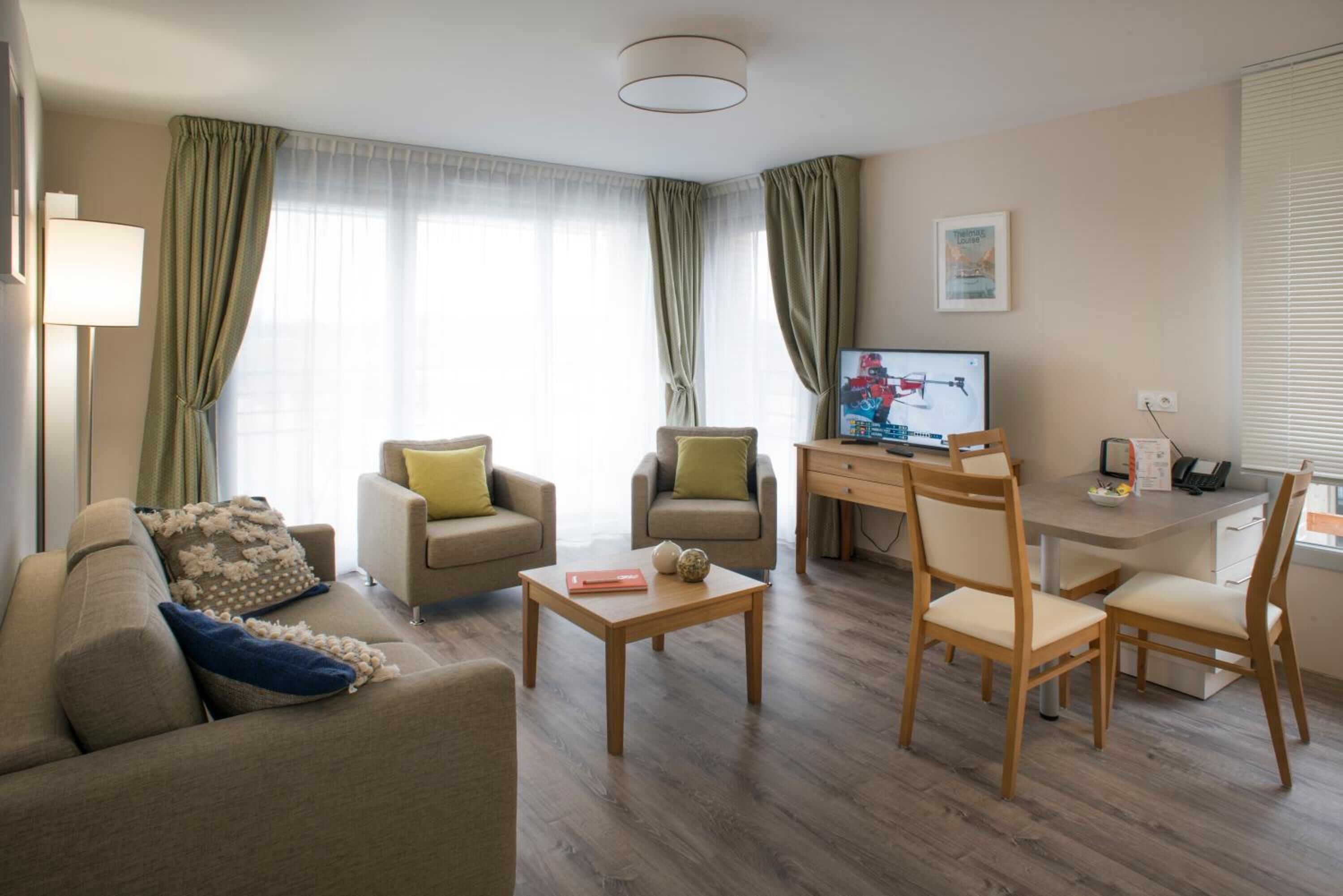 Un salon moderne comprenant un canapé, deux fauteuils, une table basse, un téléviseur et un bureau avec des chaises.