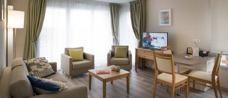 A modern living room with a sofa, two armchairs, a coffee table, a TV, and a desk with chairs.