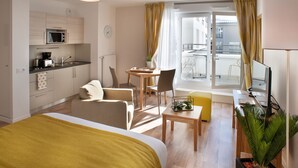 Een moderne hotelkamer met een bed, een bureau, een stoel, een klein tafeltje, een magnetron, een wastafel en een balkon met gordijnen.