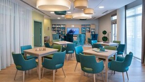 Een moderne bibliotheek met smaragdgroene stoelen en tafels, boekenplanken en een televisiescherm.