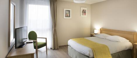 Una habitación de hotel con una cama, un escritorio con computadora, una silla y un televisor.