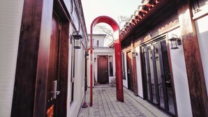 A narrow corridor with traditional wooden doors and a red archway. - HongYi Home (Beijing)