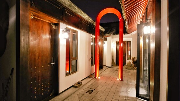 A corridor with wooden doors and a red archway, leading to rooms with visible windows and a tiled floor. - HongYi Home (Beijing)