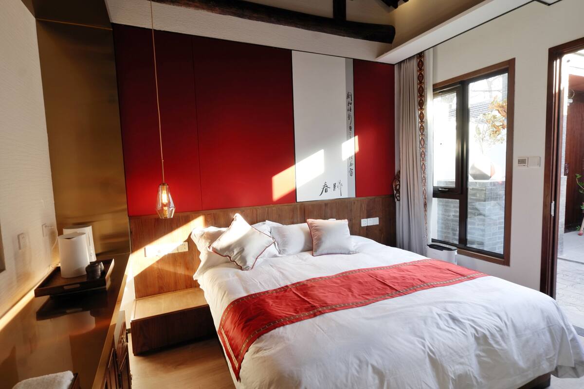 A modern bedroom with a large bed, a wooden headboard, and a red accent wall.