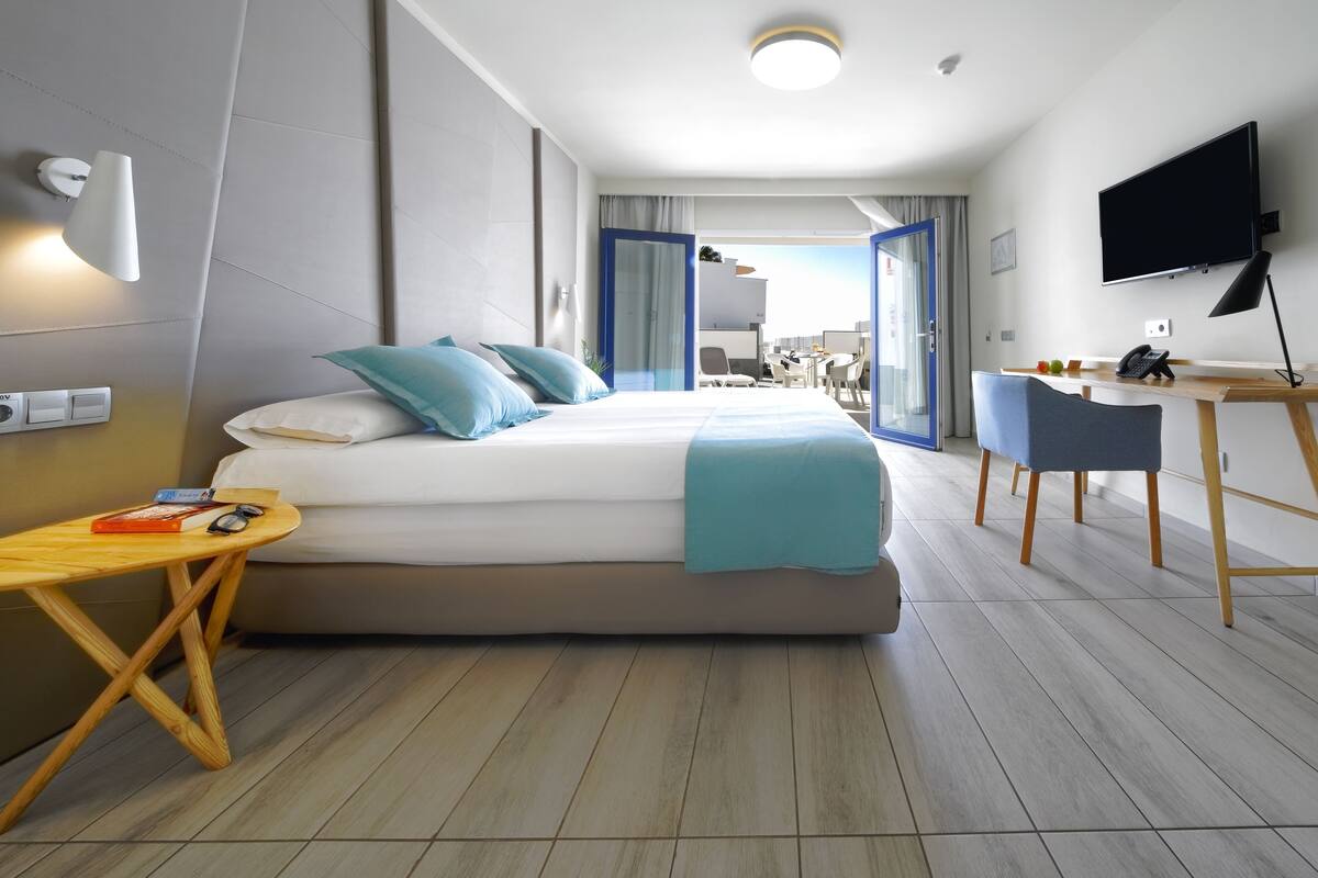Habitación de hotel moderna con cama, escritorio, silla, televisor y vistas al exterior.