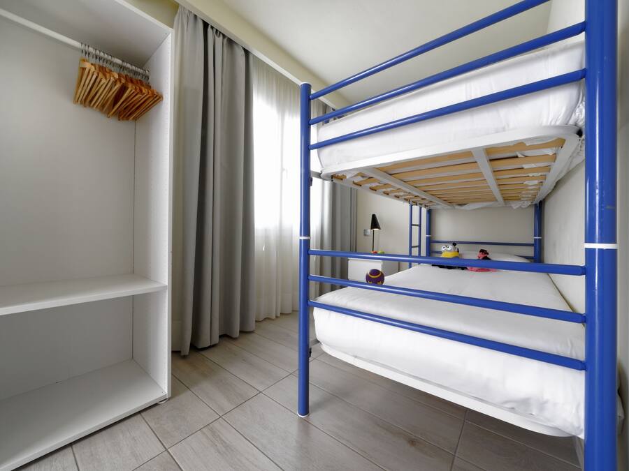 Una cama nido con barandillas azules, un armario blanco y un espejo en la pared.