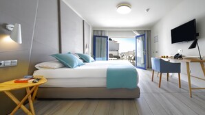 Una habitación de hotel moderna con una cama grande, un escritorio, una silla, un televisor y un balcón con vistas.