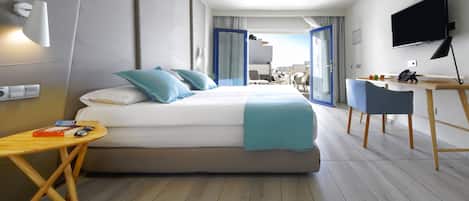A modern hotel room with a large bed, a desk, a chair, a TV, and a balcony with a view.
