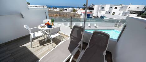 Un balcon avec deux fauteuils, une table garnie de fruits et une vue sur la mer et les bâtiments blancs.