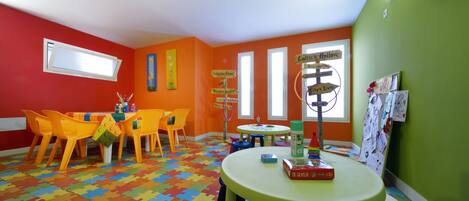 A brightly colored room with orange and green walls, a puzzle-patterned floor, and a table with chairs.
