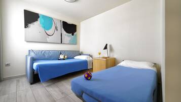 A room with two beds, a sofa, a wall art piece, and a nightstand with a lamp.
