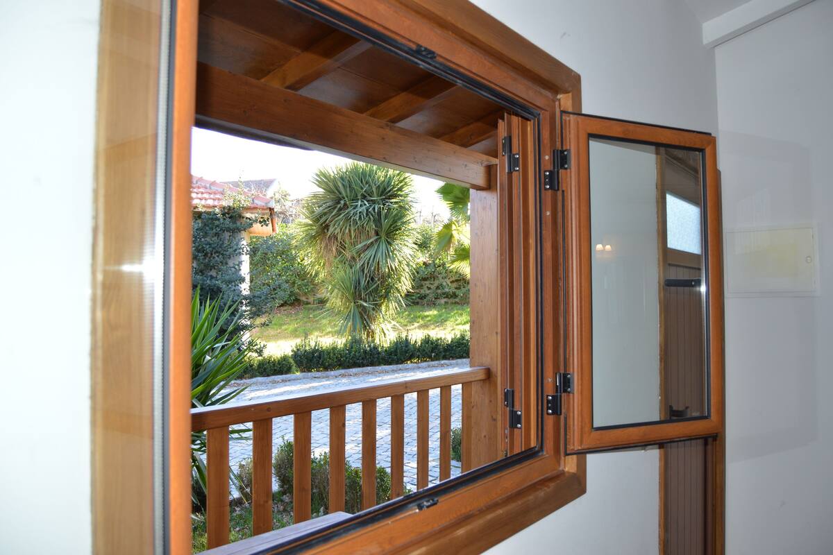 A wooden-framed window with a view of a garden and a building in the background.