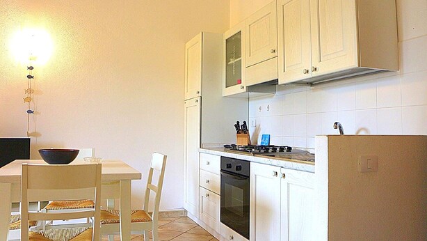 Una cocina compacta con armarios blancos, estufa, horno y comedor con mesa y sillas.