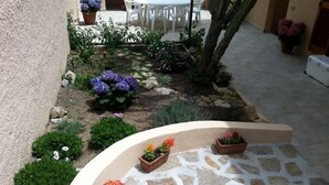 A stone-tiled patio with a curved wall, surrounded by various potted plants and flowers. - Residenza del Comandante (Santa Teresa di Gallura)