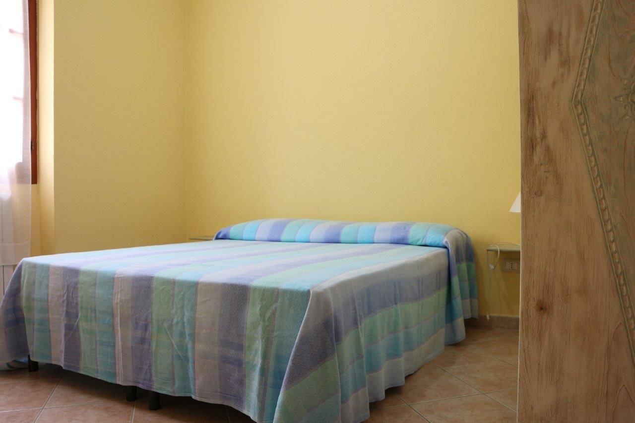 A single bed with a striped bedspread in a room with yellow walls and a wooden door.