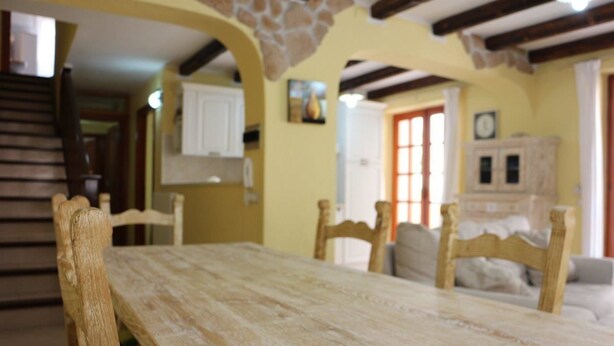 A dining area with a wooden table and chairs, a staircase, and a kitchen in the background. - Residenza del Comandante (Santa Teresa di Gallura)