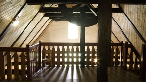 A wooden attic room with a sloped ceiling, a wooden railing, and a single chair. - Gästehaus Klein Grönau (Lübeck)