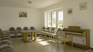 A room with a piano, a long table, and chairs arranged around it. - Gästehaus Klein Grönau (Lübeck)