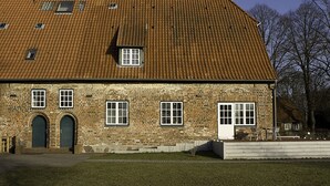 A brick building with a tiled roof, multiple windows, and a small door. - Gästehaus Klein Grönau (Lübeck)