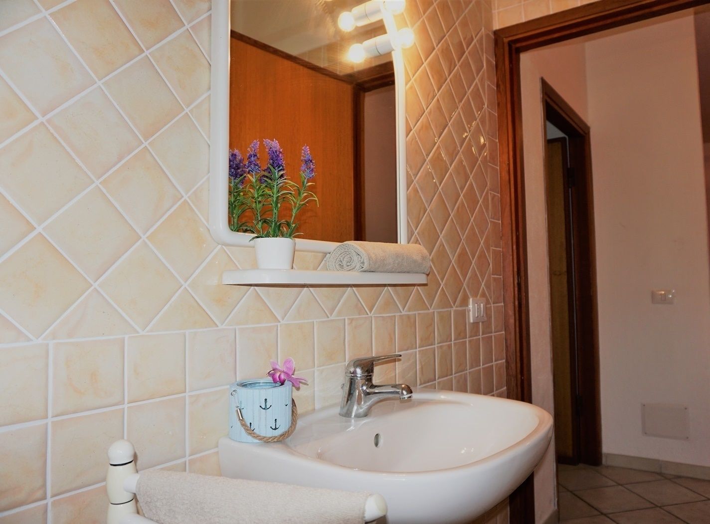 A bathroom with a white sink, a mirror, and a shelf with a potted plant and a towel.