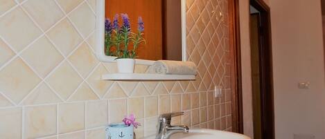 A bathroom with a white sink, a mirror, and a shelf with a potted plant and a towel.