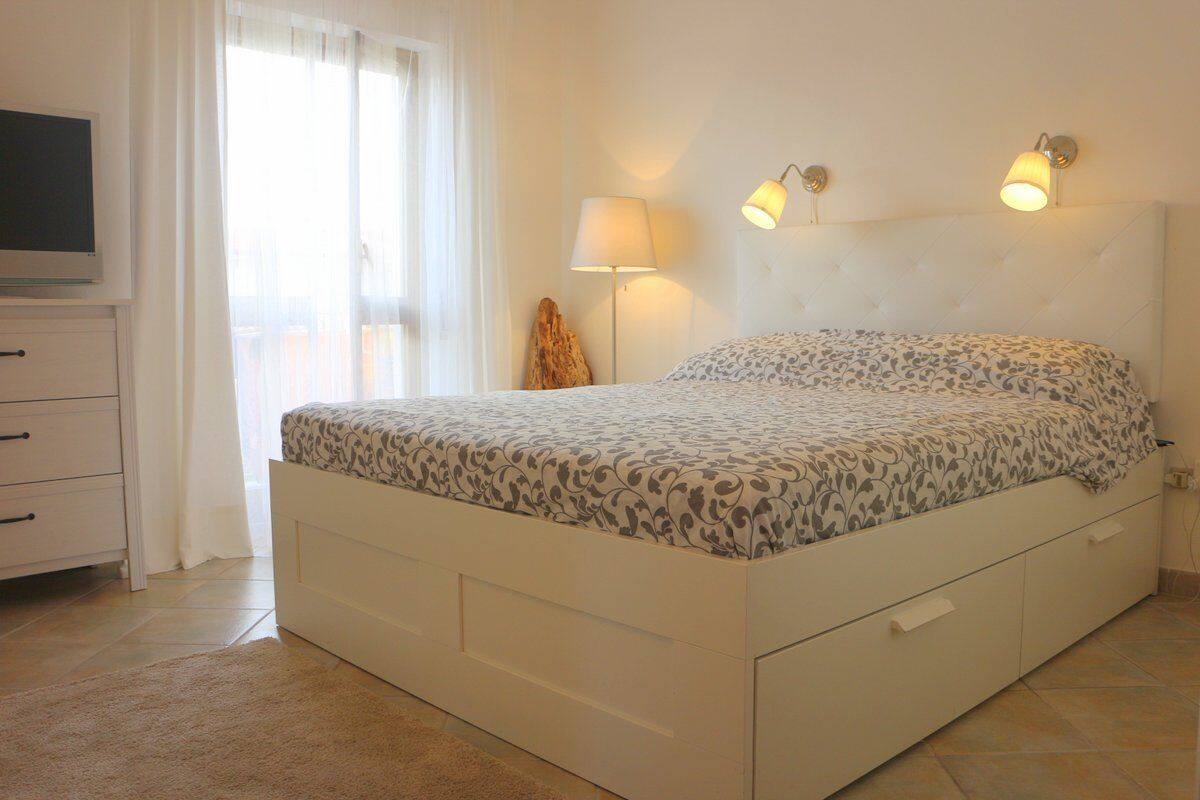 A bedroom with a bed, a bedside lamp, a TV, and a window with curtains.