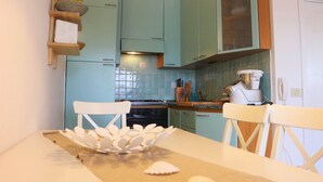 A kitchen with teal cabinets, a white countertop, and a white chair. - Residence Ostro (Santa Teresa di Gallura)